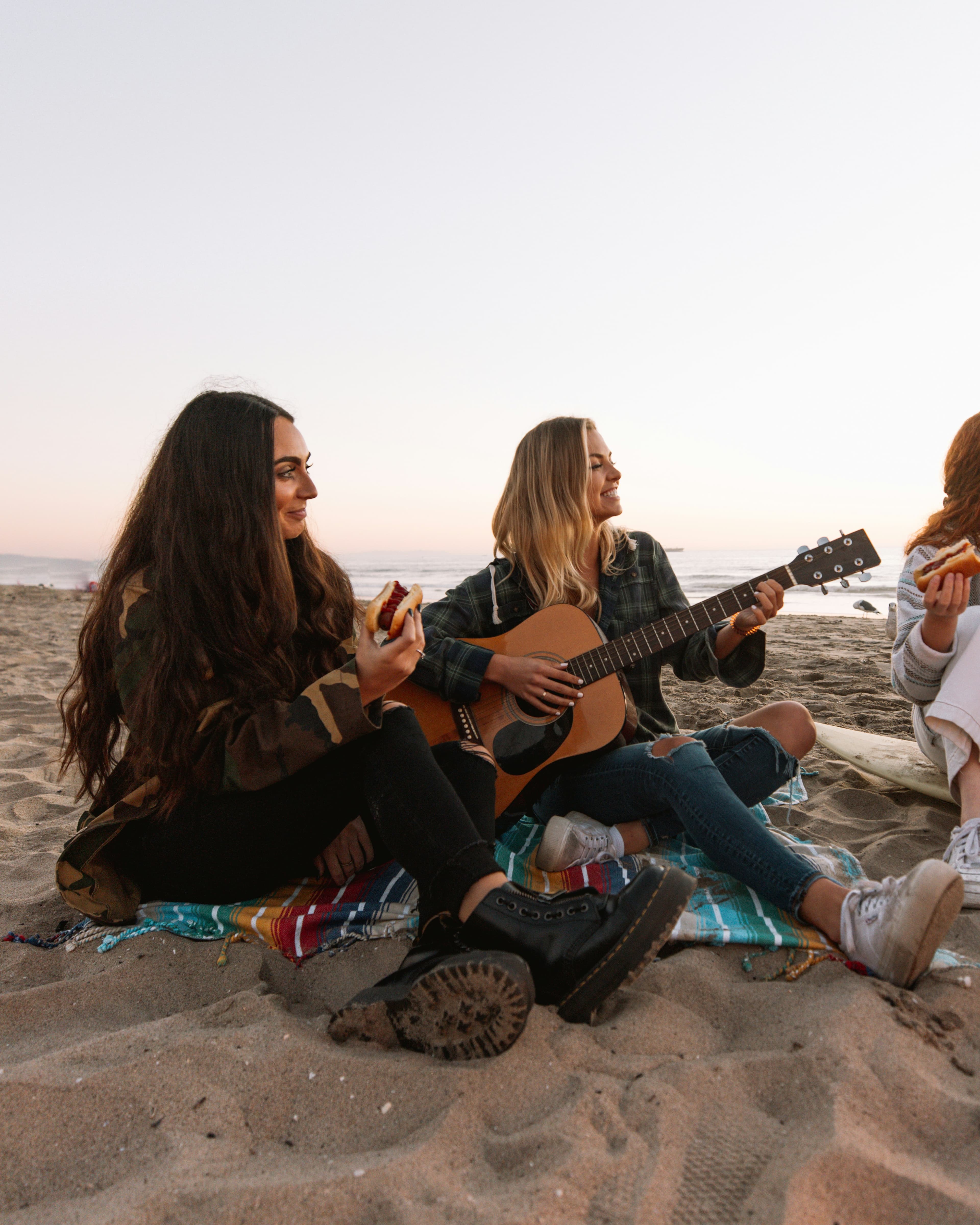Woman playing guitar on a beach with friends